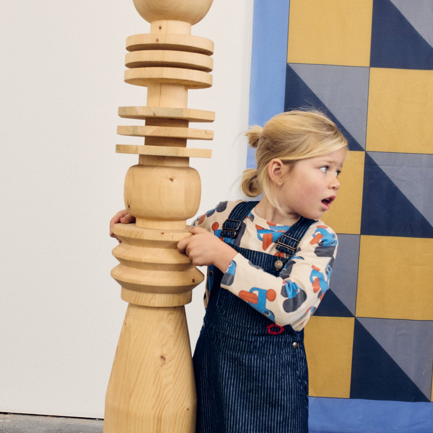 Child playing with a wooden tower toy against a colorful geometric-patterned wall.