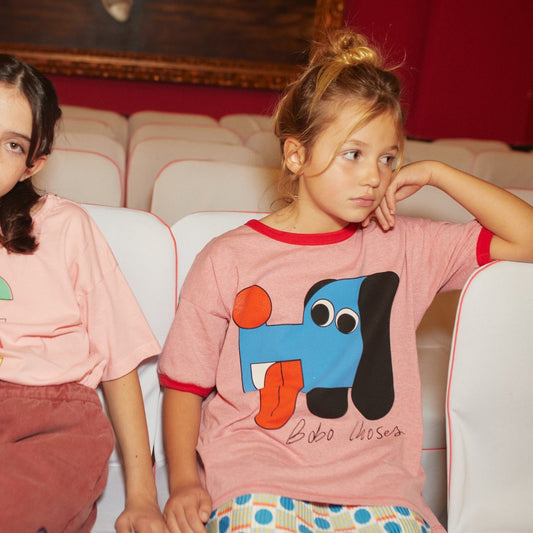 Two children sitting on a white couch wearing pink t-shirts with colorful designs.