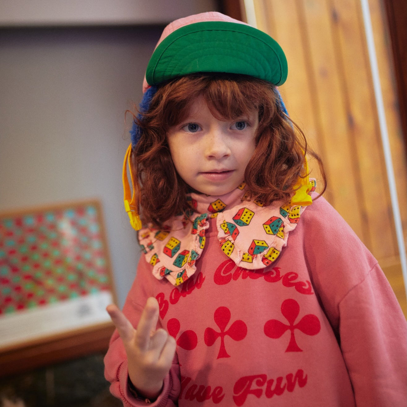 Child wearing a colorful outfit with a pink sweater and green visor in an indoor setting