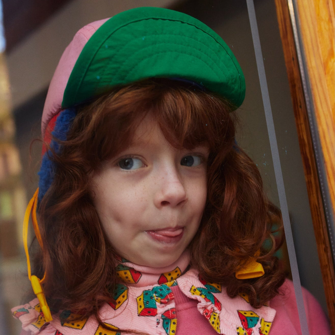 Person wearing a colorful outfit with a green hat and pink floral dress.