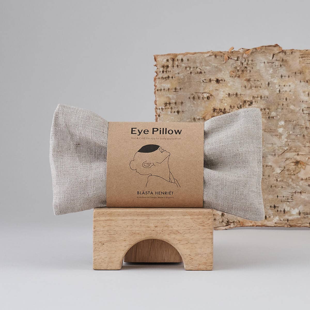Blästa Henriët eye pillow in plain linen, displayed in eco-friendly packaging on a wooden stand with a natural birch backdrop.
