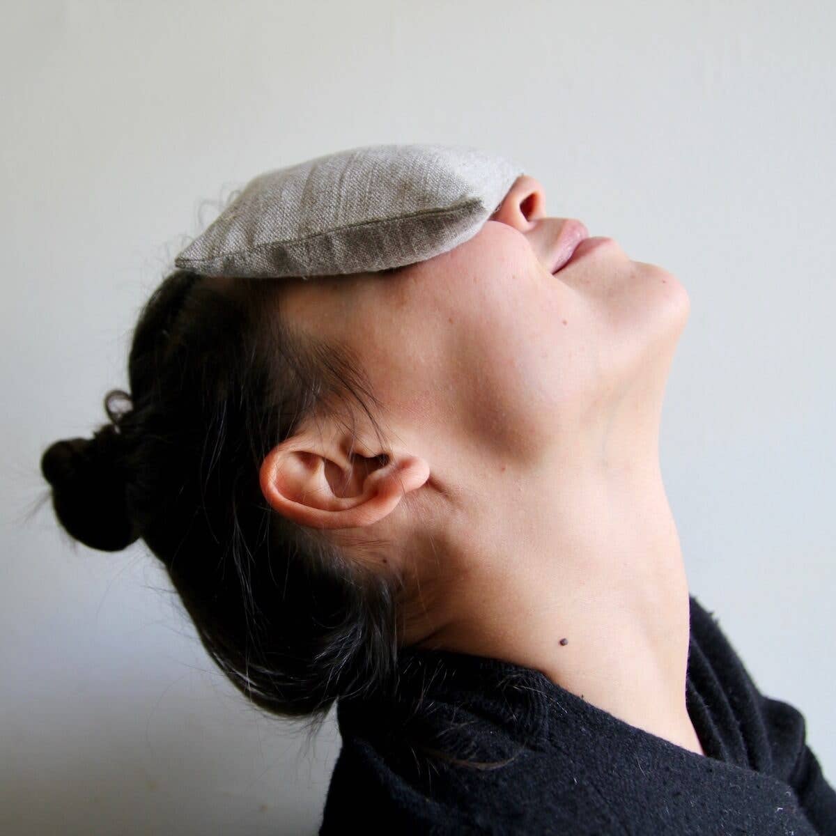 Person reclining with a plain linen eye pillow placed over their eyes, providing a soothing and relaxing experience