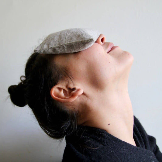 Person reclining with a plain linen eye pillow placed over their eyes, providing a soothing and relaxing experience
