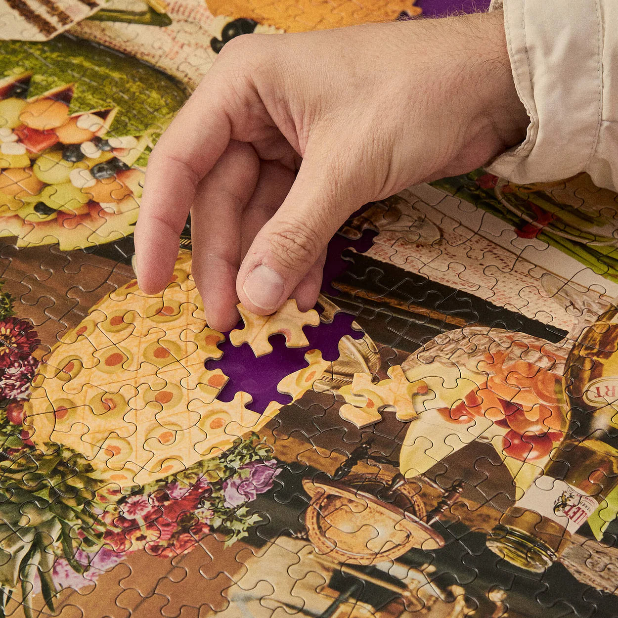 Hand placing a puzzle piece on a colorful puzzle with a scenic design.