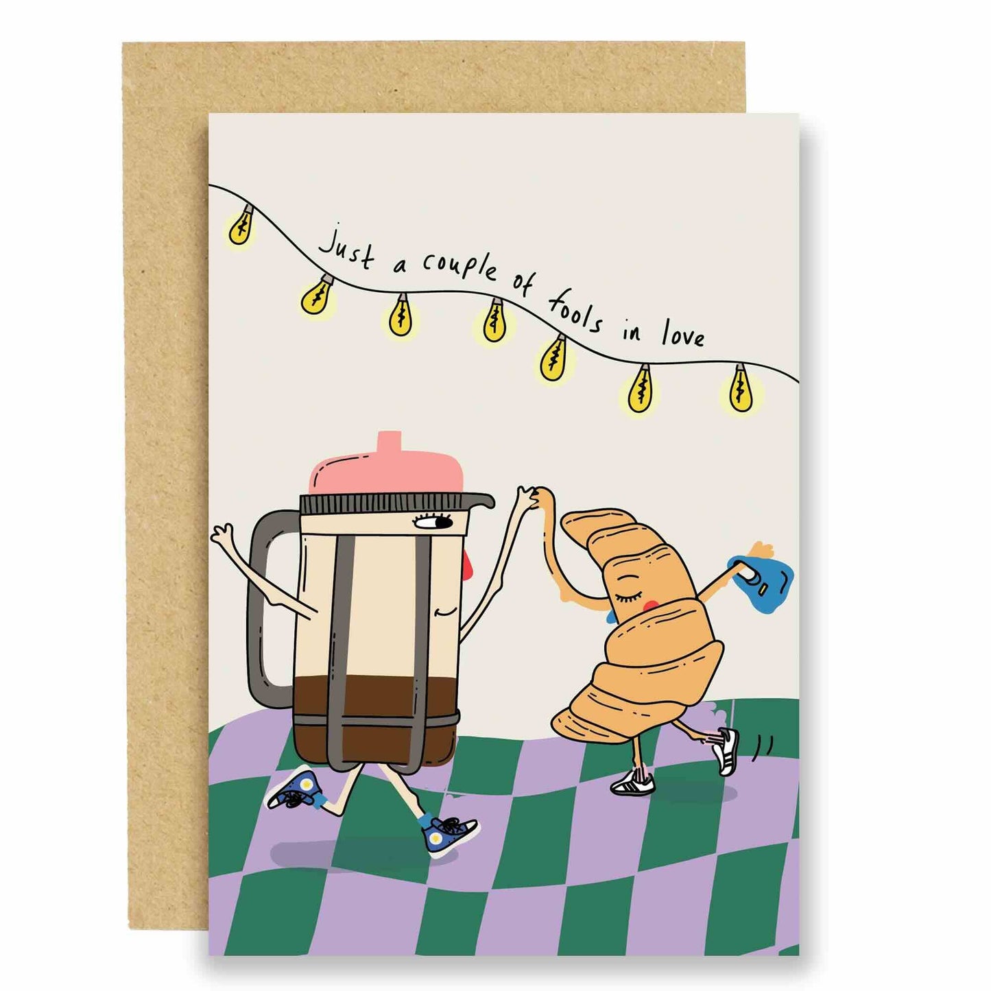 A playful greeting card with an illustration of a coffee pot and a croissant dancing, accompanied by the phrase 'Just a couple of fools in love'.