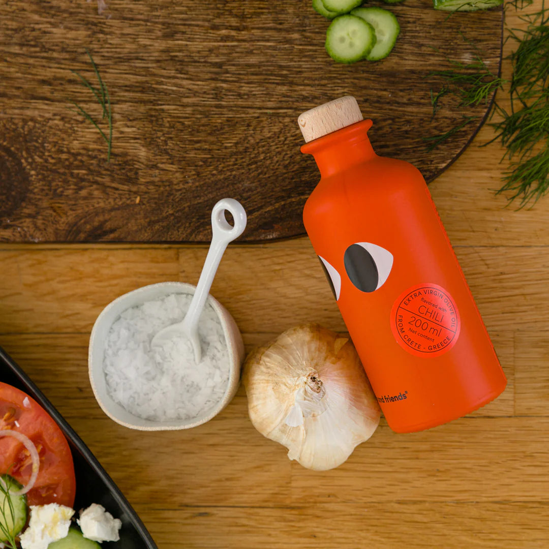 Orange bottle with a face design on a wooden table with vegetables and a bowl.