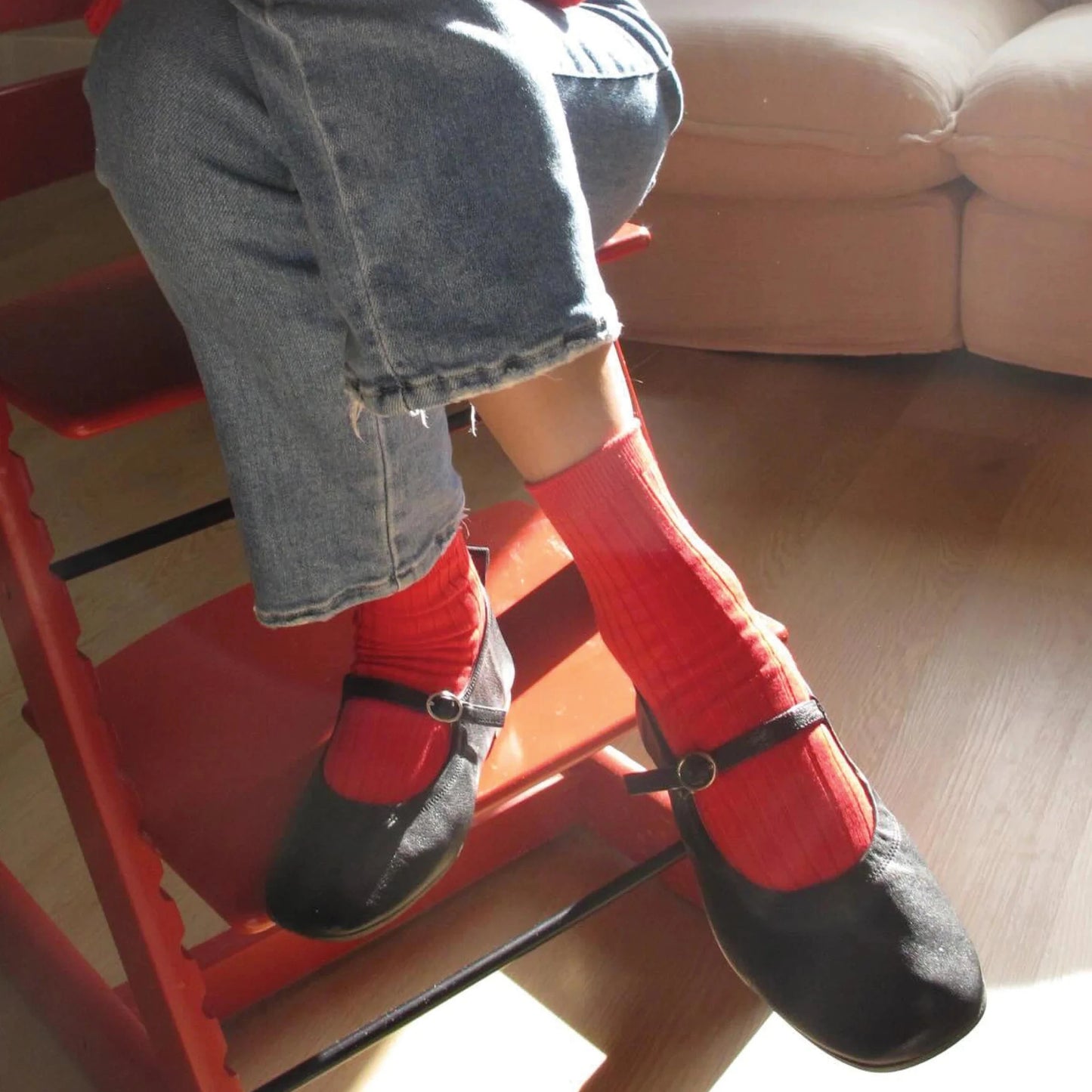 Person wearing red socks and black shoes sitting on a red chair indoors.