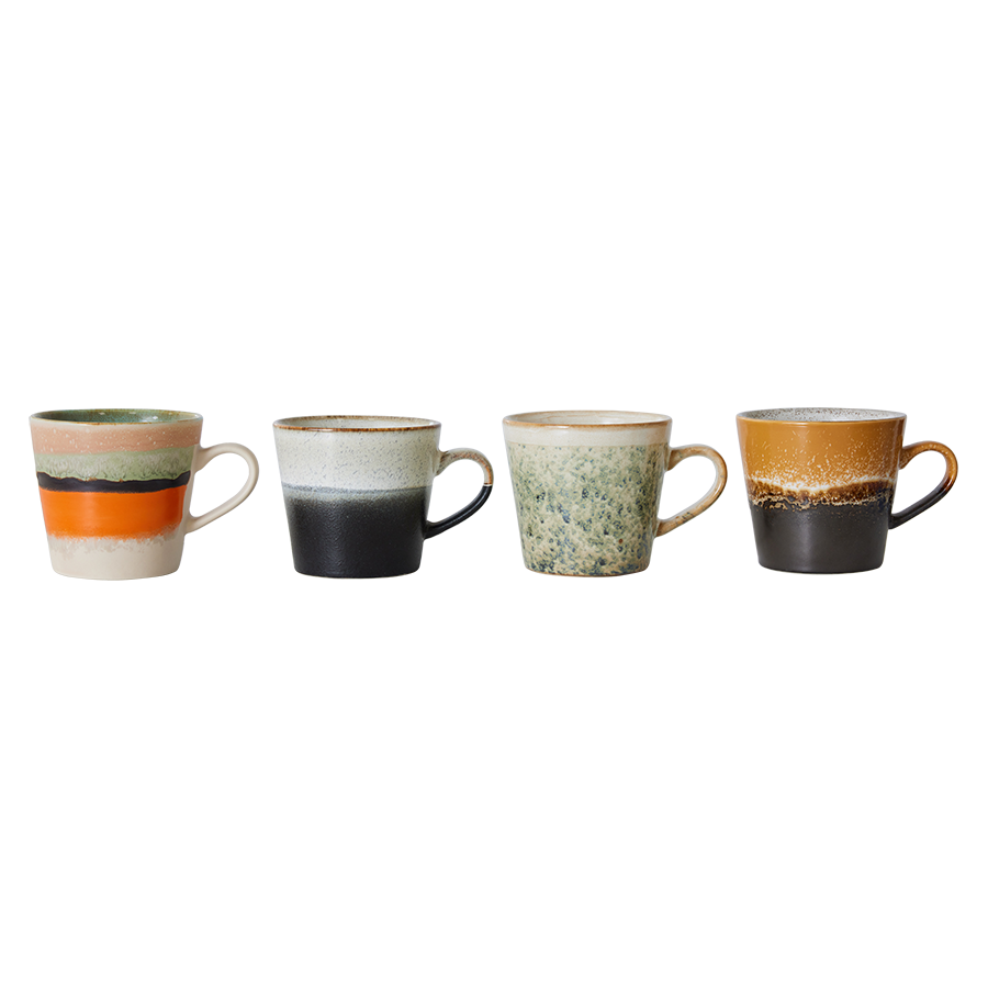Set of four hkliving verve cappuccino mugs. The first is half grey then has a short fade to a speckled white. Next one is a mug with half orange and stripes of black and green then cream at the top. Then there is a green spackled mug which fades fully to cream at the top. The last one is a dark brown mug with a speckled brown stripe in the middle which fades into a ochre yellow