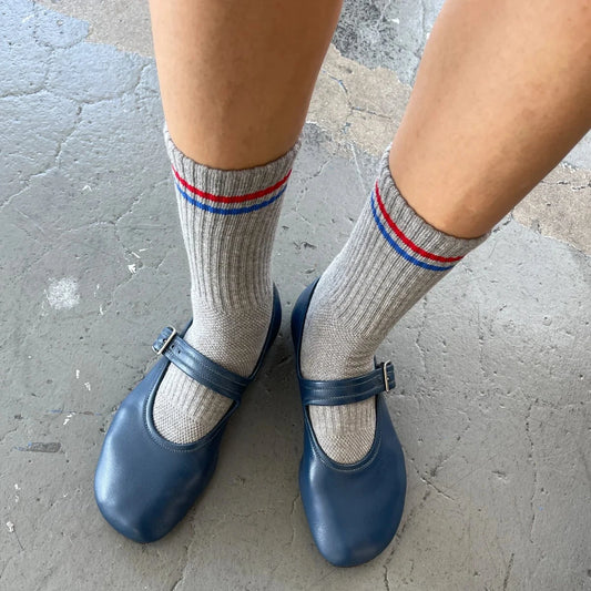 Blue shoes and gray socks with red and blue stripes on a concrete floor.