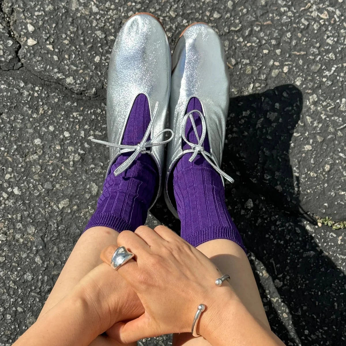 Silver shoes with purple socks on a black asphalt surface
