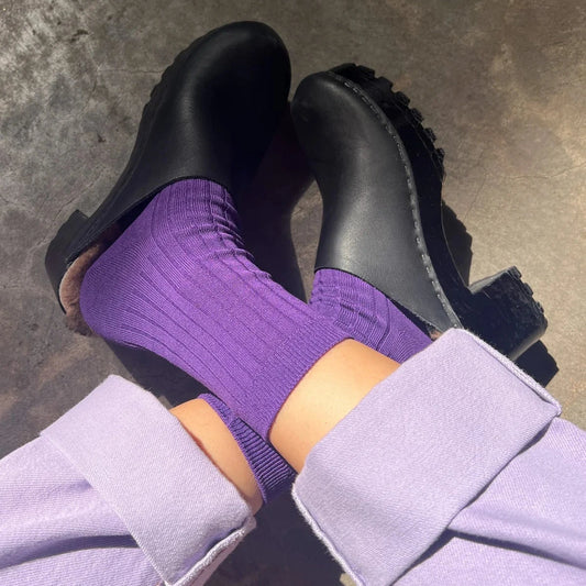 Black clogs with purple socks on a concrete floor