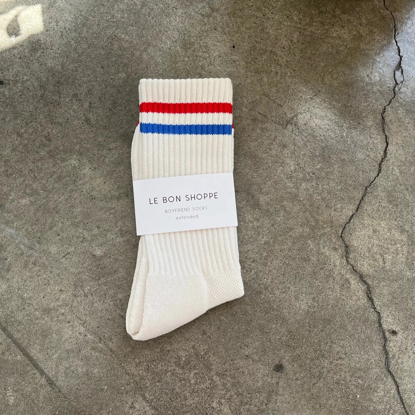 A pair of white socks with red and blue stripes on the cuff, displayed on a flat surface, with a brand label placed on top.