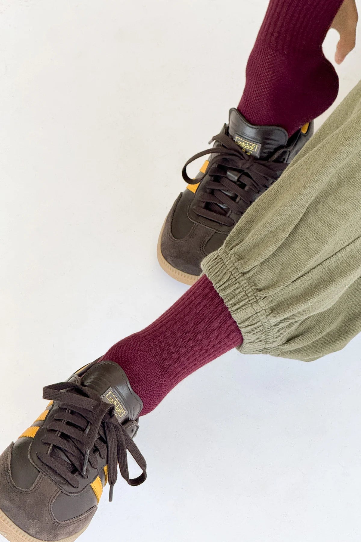 Person wearing maroon socks, green pants, and brown sneakers on a white background
