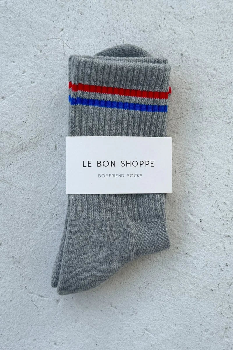 Gray socks with red and blue stripes on a textured white surface, featuring 'Le Bon Shoppe' label.