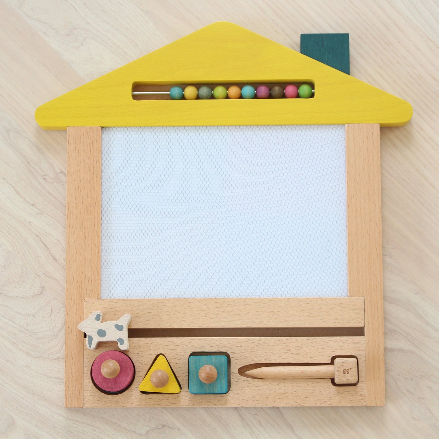 Hand-crafted wooden magnetic drawing board in the shape of a house, with a yellow front, beige body, and wooden accents. It includes a magnetic pen and various colored magnetic stamps.