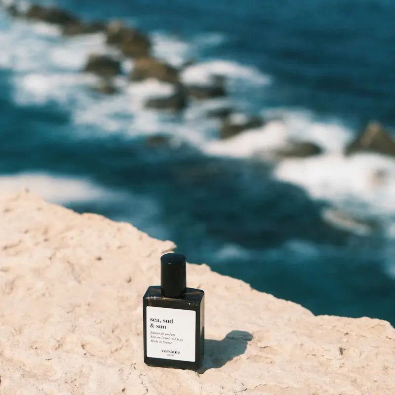 Perfume bottle labeled 'sea, sand & sun' on a rock with ocean in the background