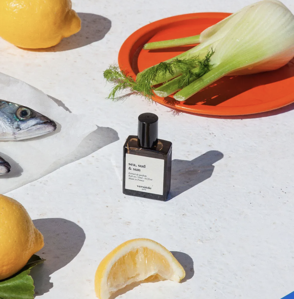 Perfume bottle with lemons, fish, and fennel on a white surface