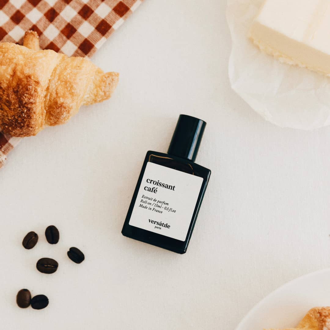 Perfume bottle labeled 'croissant cafe' with a croissant and coffee beans on a checkered tablecloth.