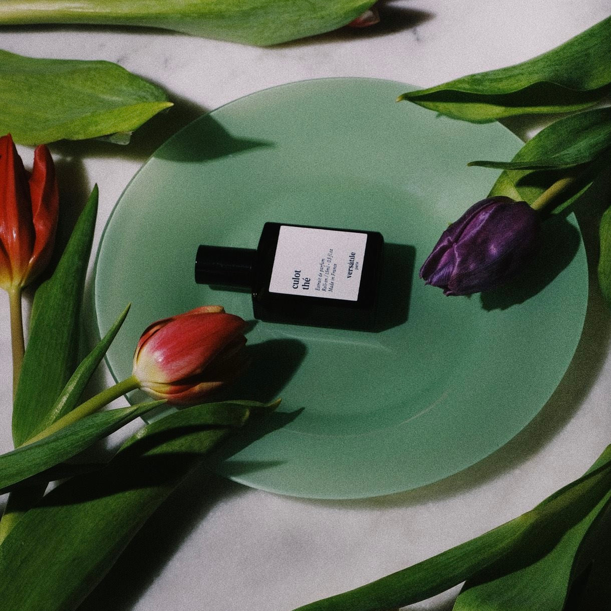 Small bottle of perfume on a green plate surrounded by tulips