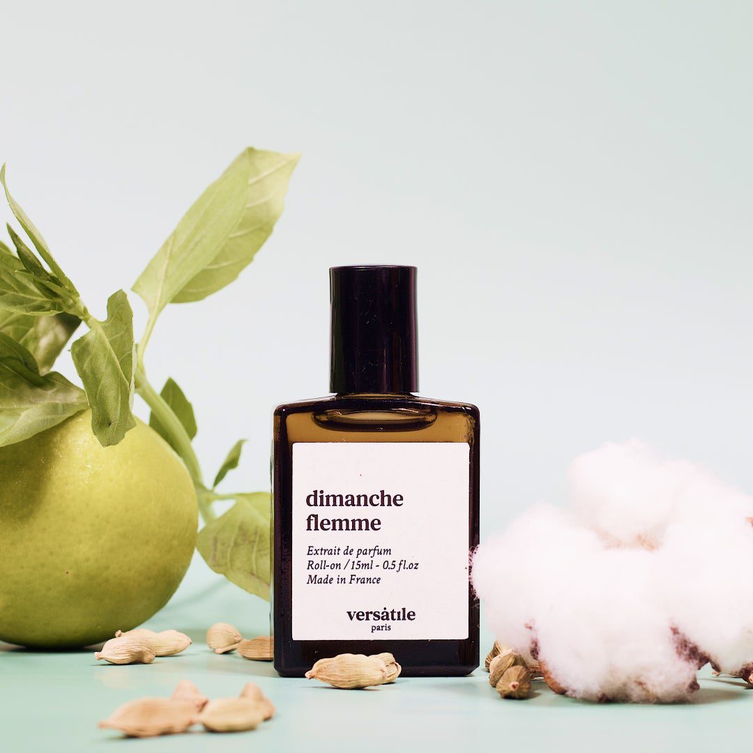 Perfume bottle labeled 'dimanche fèmme' by Versètille with green leaves and cotton in the background