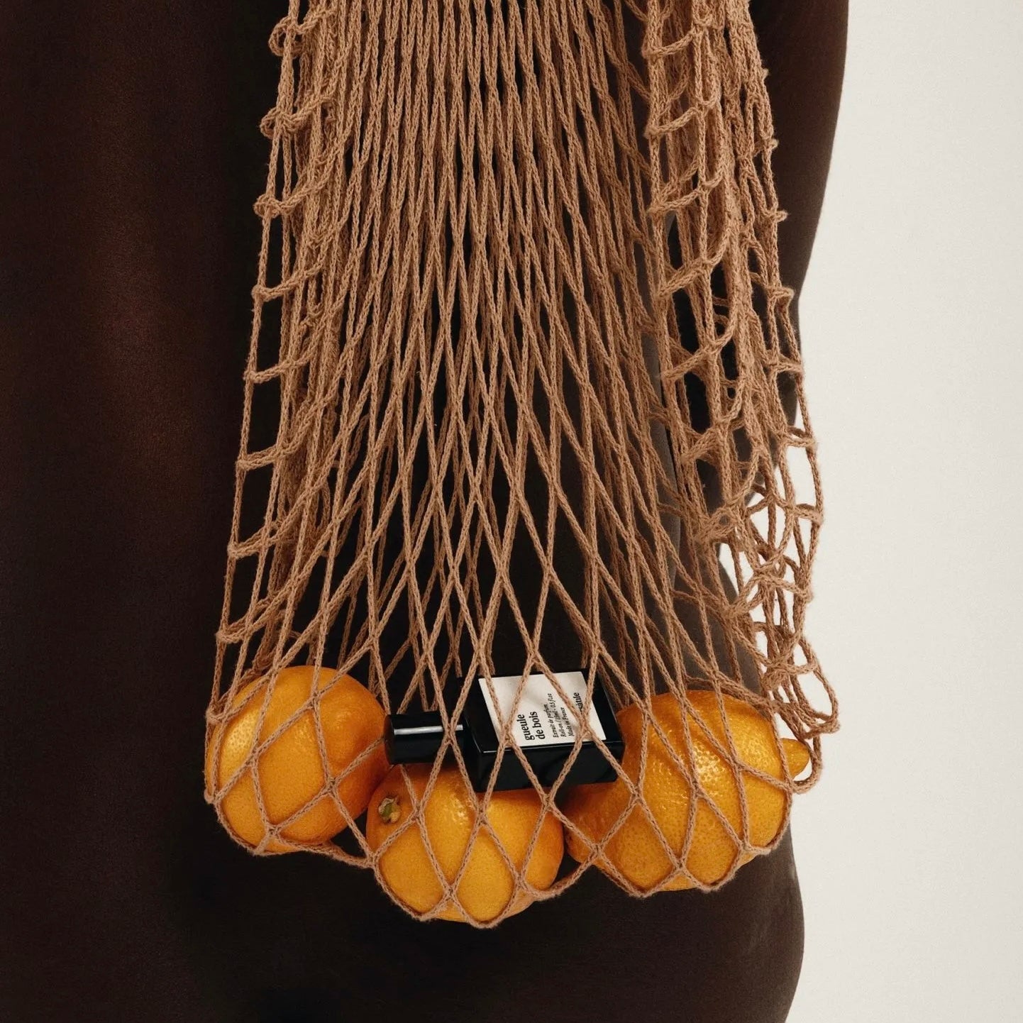 Person wearing a brown net bag filled with lemons on a plain background
