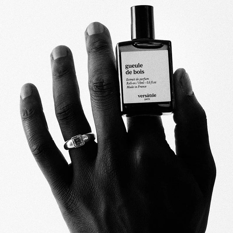 Hand holding a 'Gueule de Bois' Versatile Paris perfume bottle on a white background
