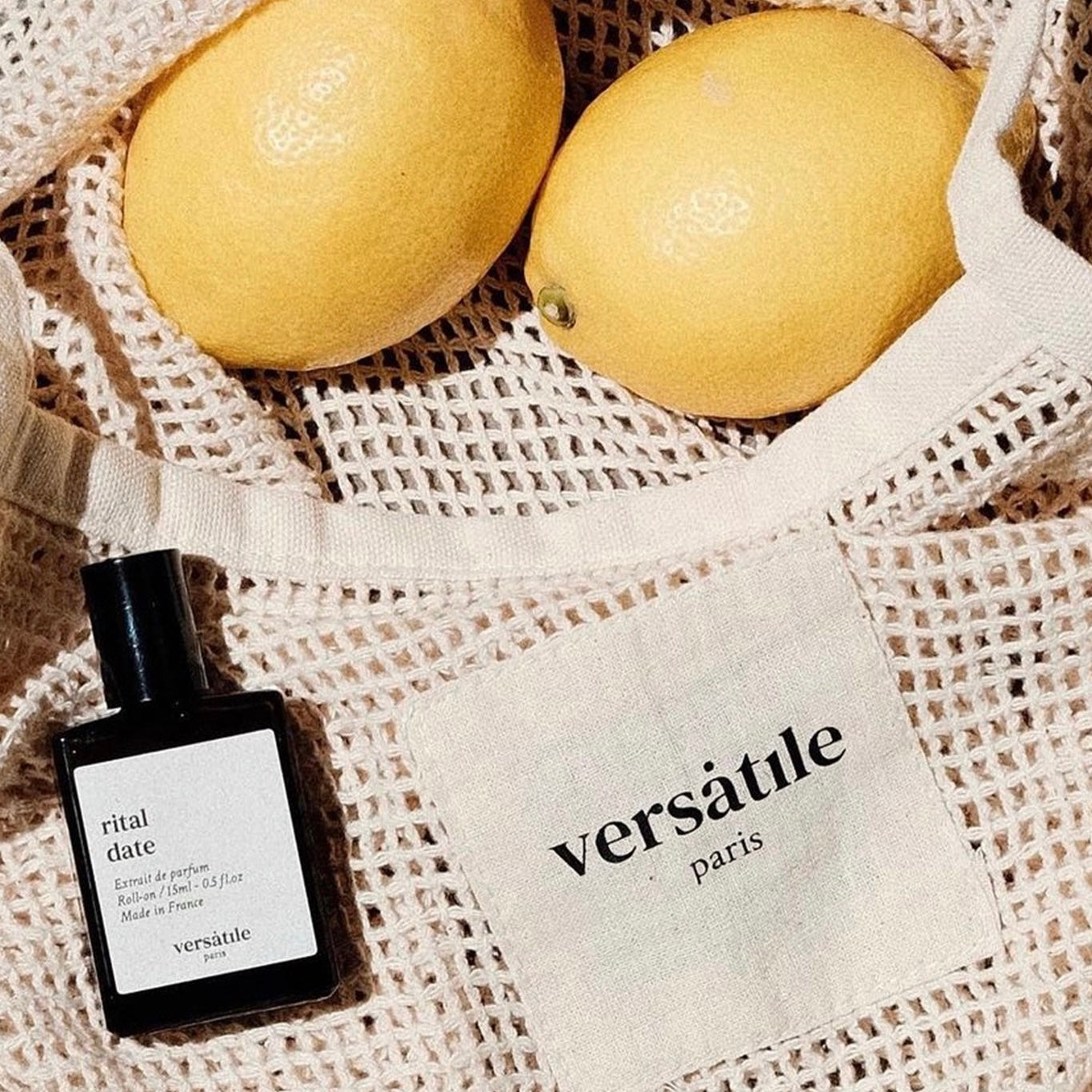 Perfume bottle labeled 'ritual date' by 'versatile paris' with two lemons on a textured surface.