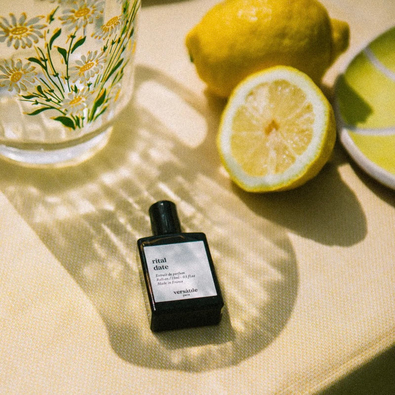 Perfume bottle labeled 'ritual date' on a table with lemons and a glass.