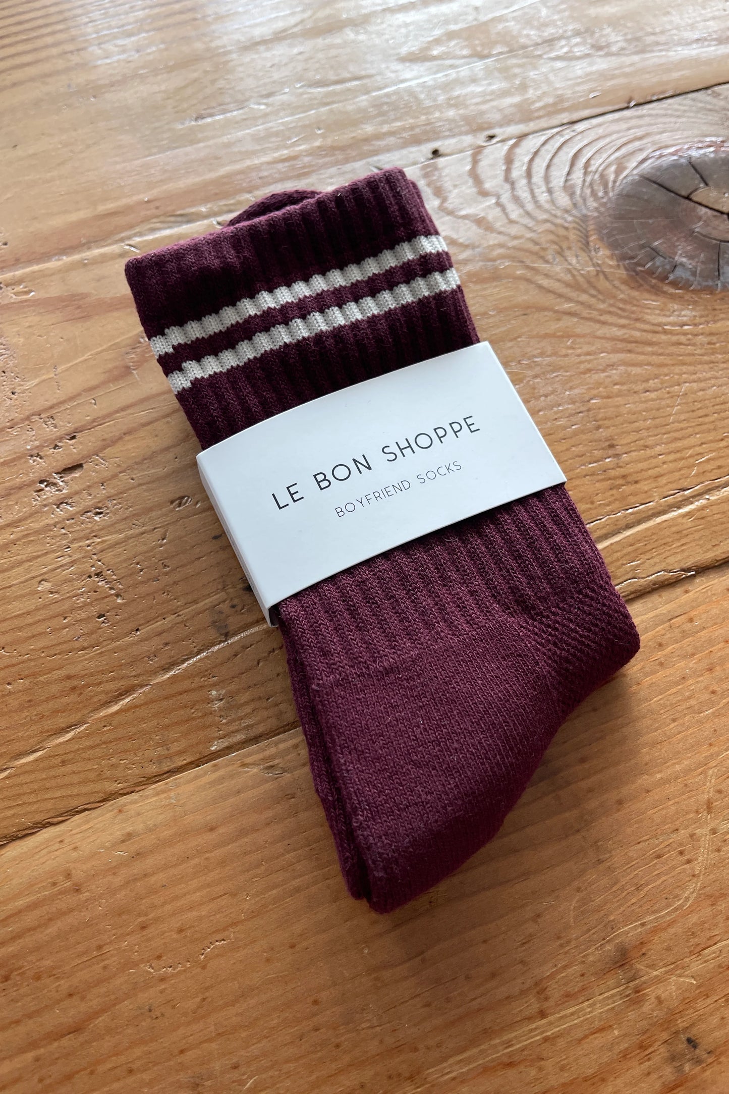 Maroon socks with white stripes on a wooden surface, branded 'Le Bon Shoppe'.