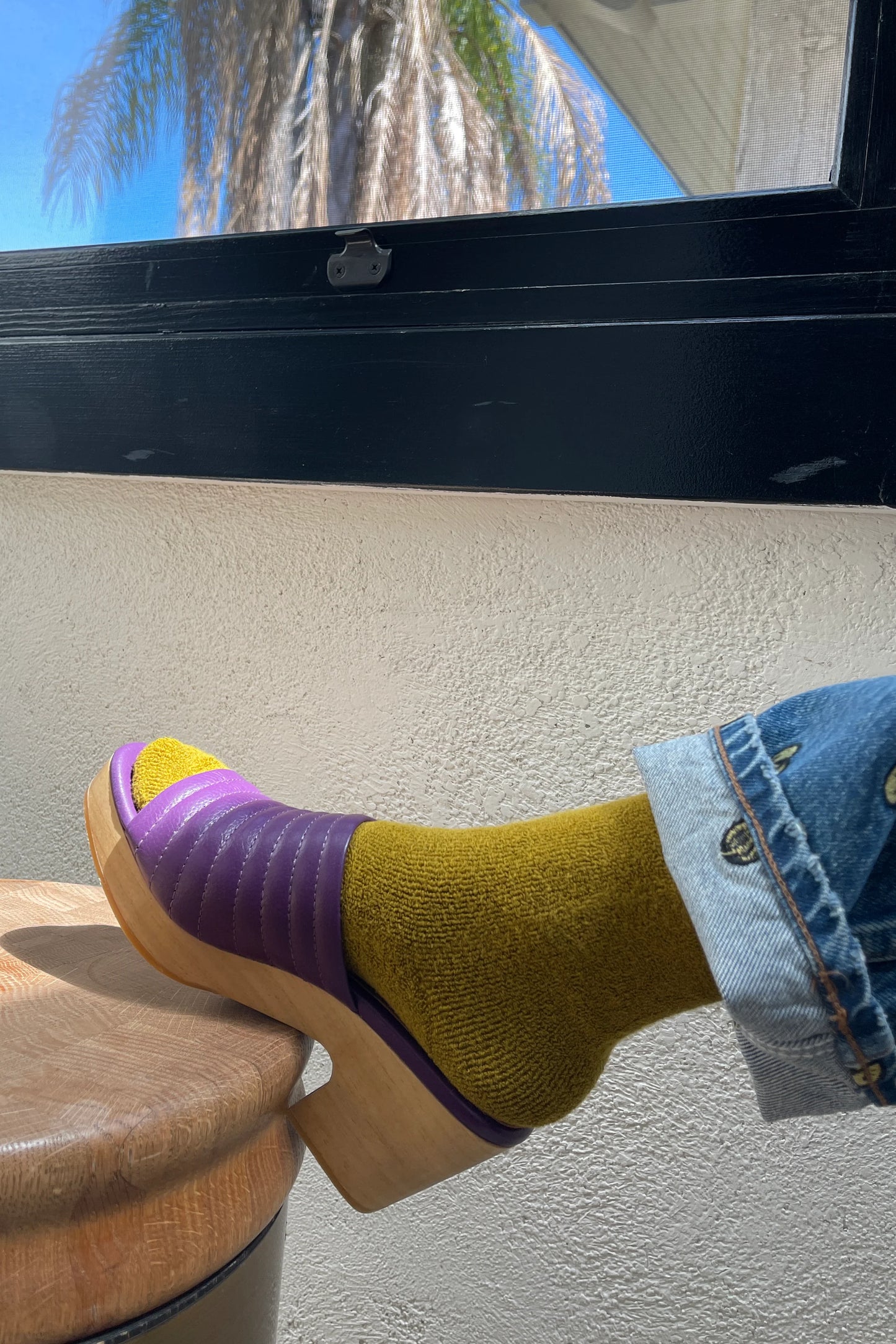 Person wearing a purple sandal and yellow sock, sitting on a chair with a palm tree in the background.