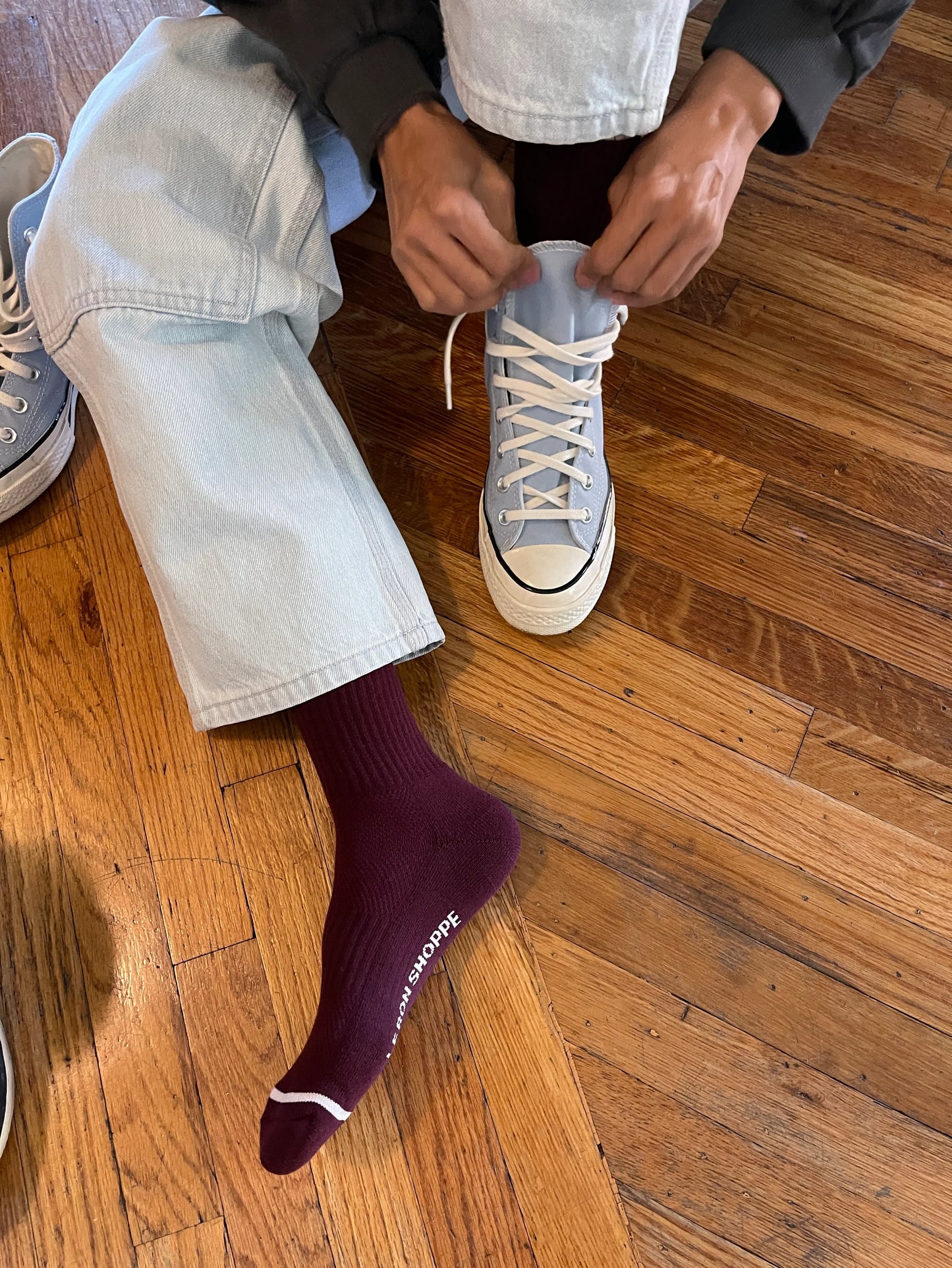 Person tying shoelaces on a light blue sneaker on a wooden floor.
