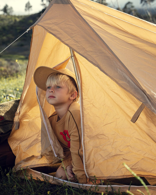Child peeking out from a beige tent in an outdoor setting
