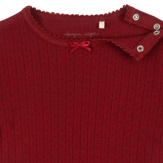 Close-up of the neckline of the Konges Sløjd Red Dahlia Newborn Minnie Body, showcasing the lace trim, ribbed texture, and snap button closure for easy dressing.