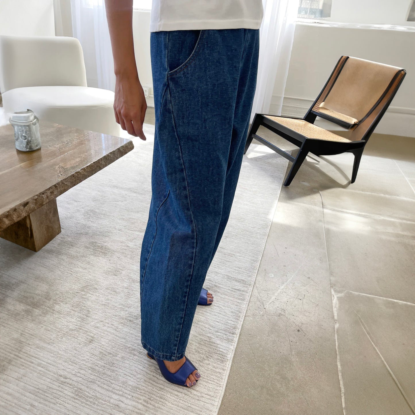 A pair of stylish high-waisted Arc Pants made from heavyweight denim, featuring a cropped length and slightly curved leg shape. The design includes unique side panels and deep pockets, perfect for casual wear. A side view with the model wearing a white t-shirt with the pants