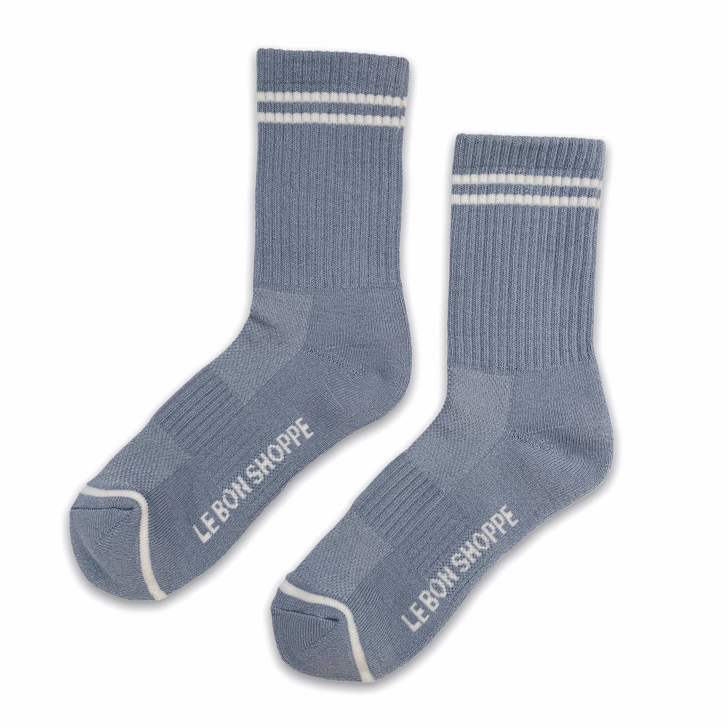 A pair of ribbed light blue socks with white stripes at the cuffs and white "Le Bon Shoppe" branding on the foot, laid flat on a clean white background.