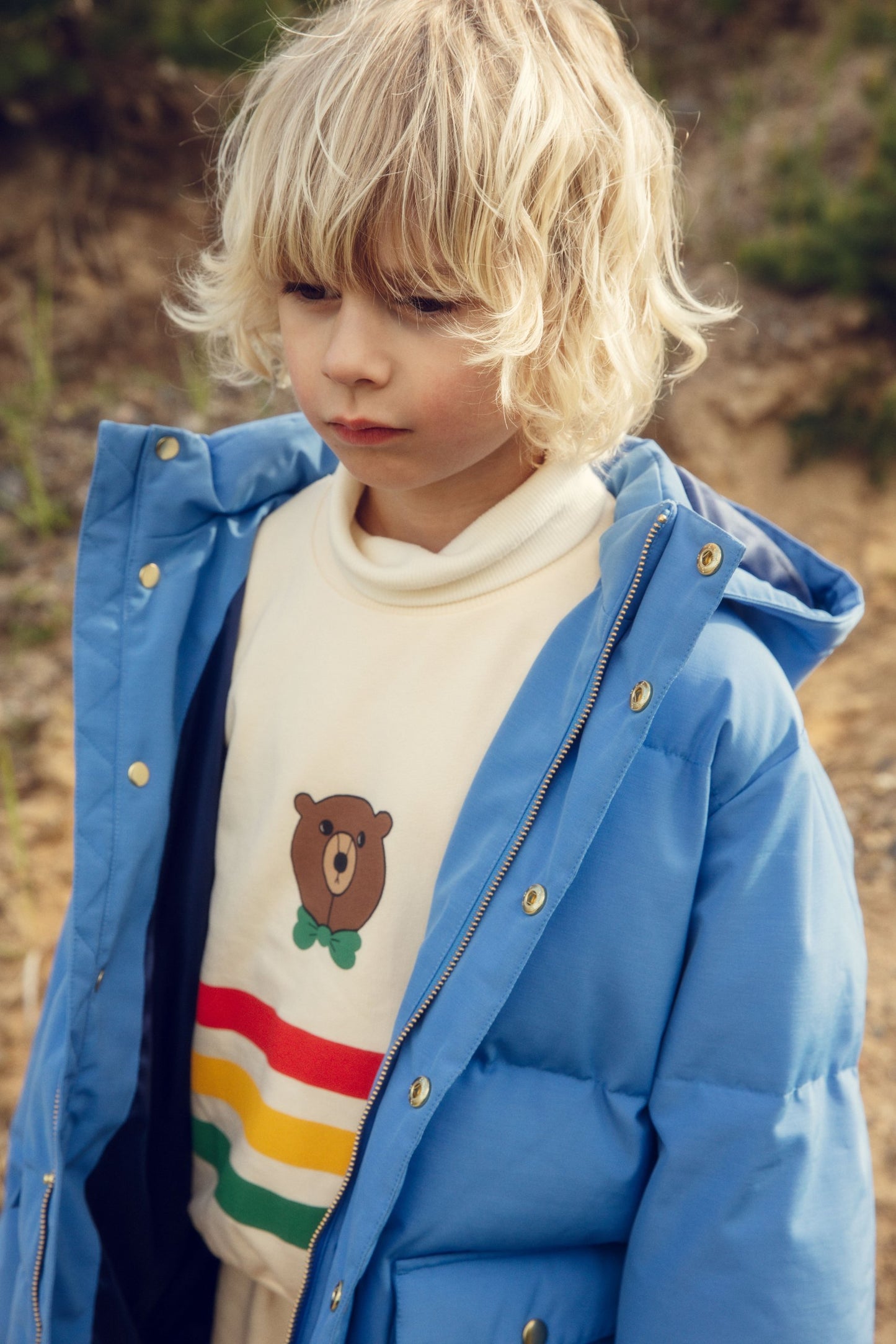 Child wearing a blue puffer jacket over a sweater with a bear design outdoors.