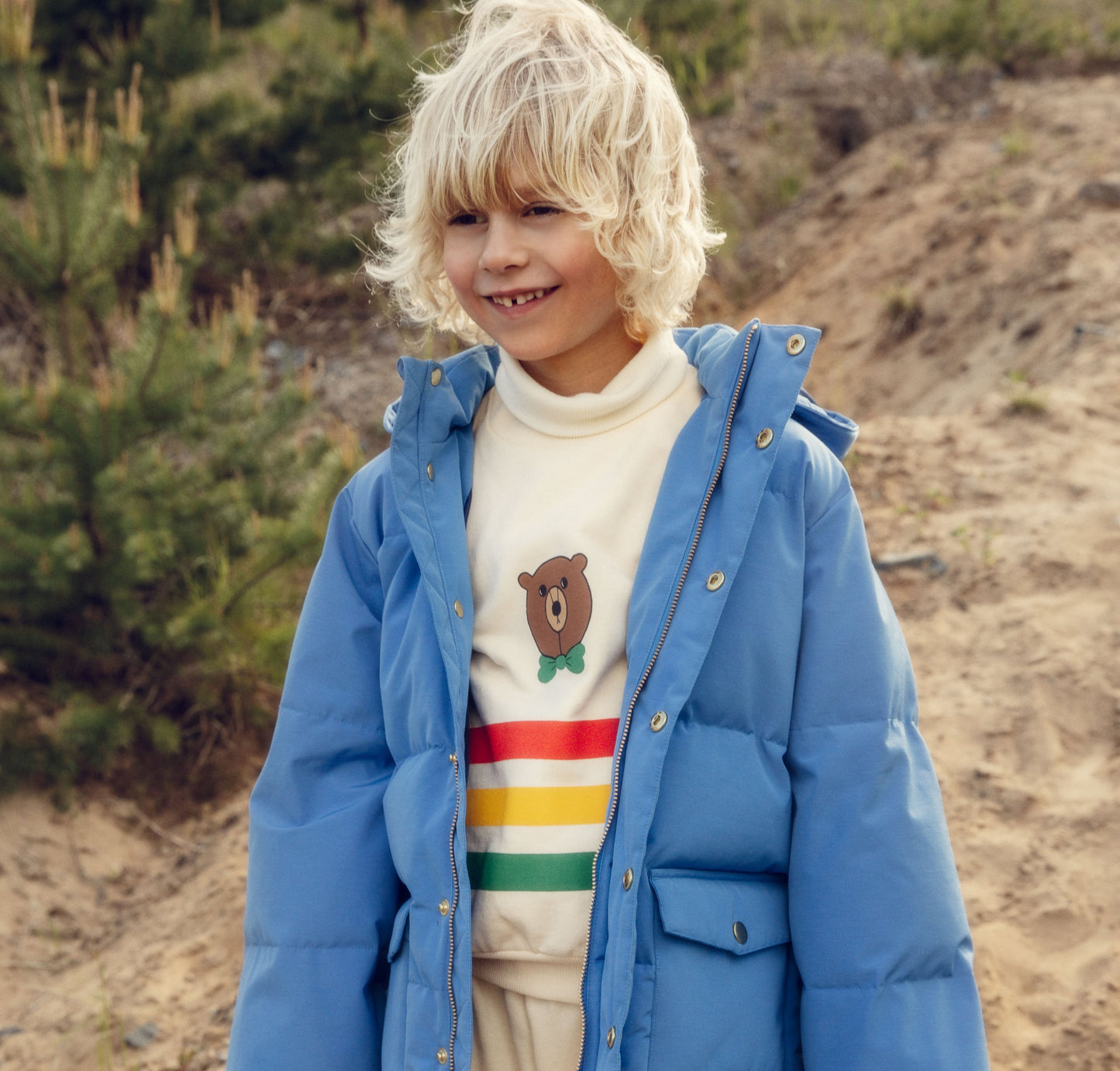 Child wearing a blue puffer jacket with a bear design in the background