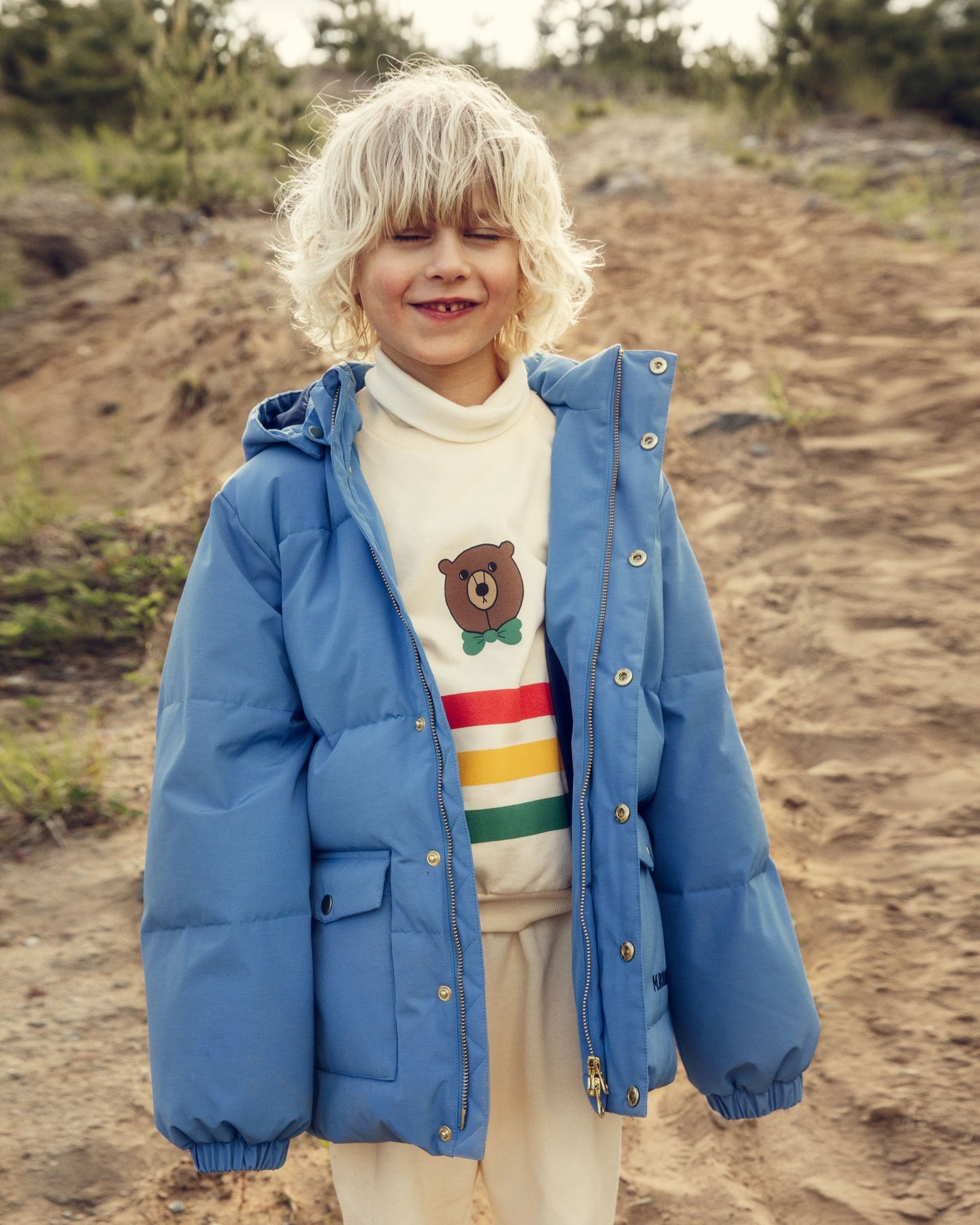 Child wearing a blue puffer jacket and a sweater with a bear design outdoors.
