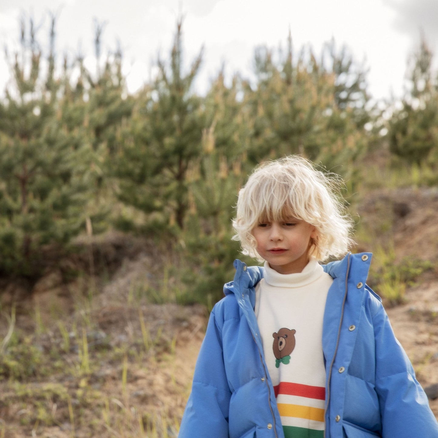 Child wearing a blue jacket and colorful sweater standing in a forest