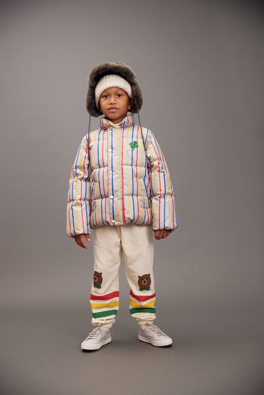 Child wearing a colorful winter outfit with a striped puffer jacket and patterned pants on a gray background