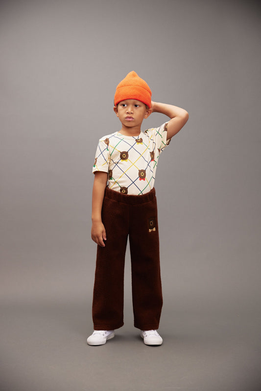 Child wearing an orange beanie, patterned shirt, and brown pants on a gray background