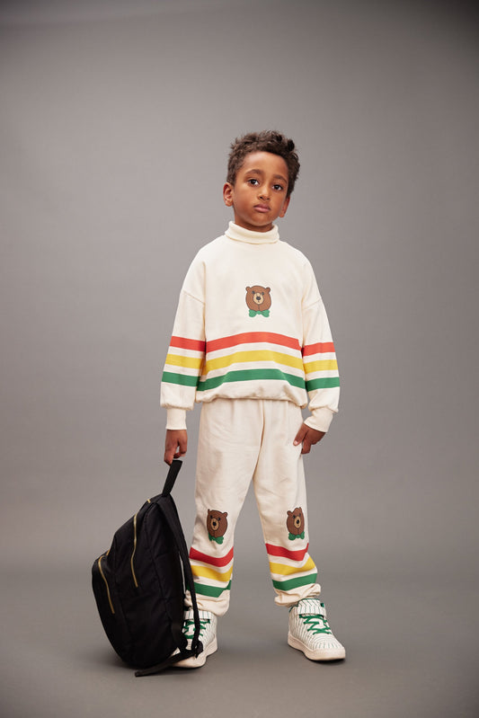 Child wearing a colorful sweater and pants with a bear design, standing against a gray background.