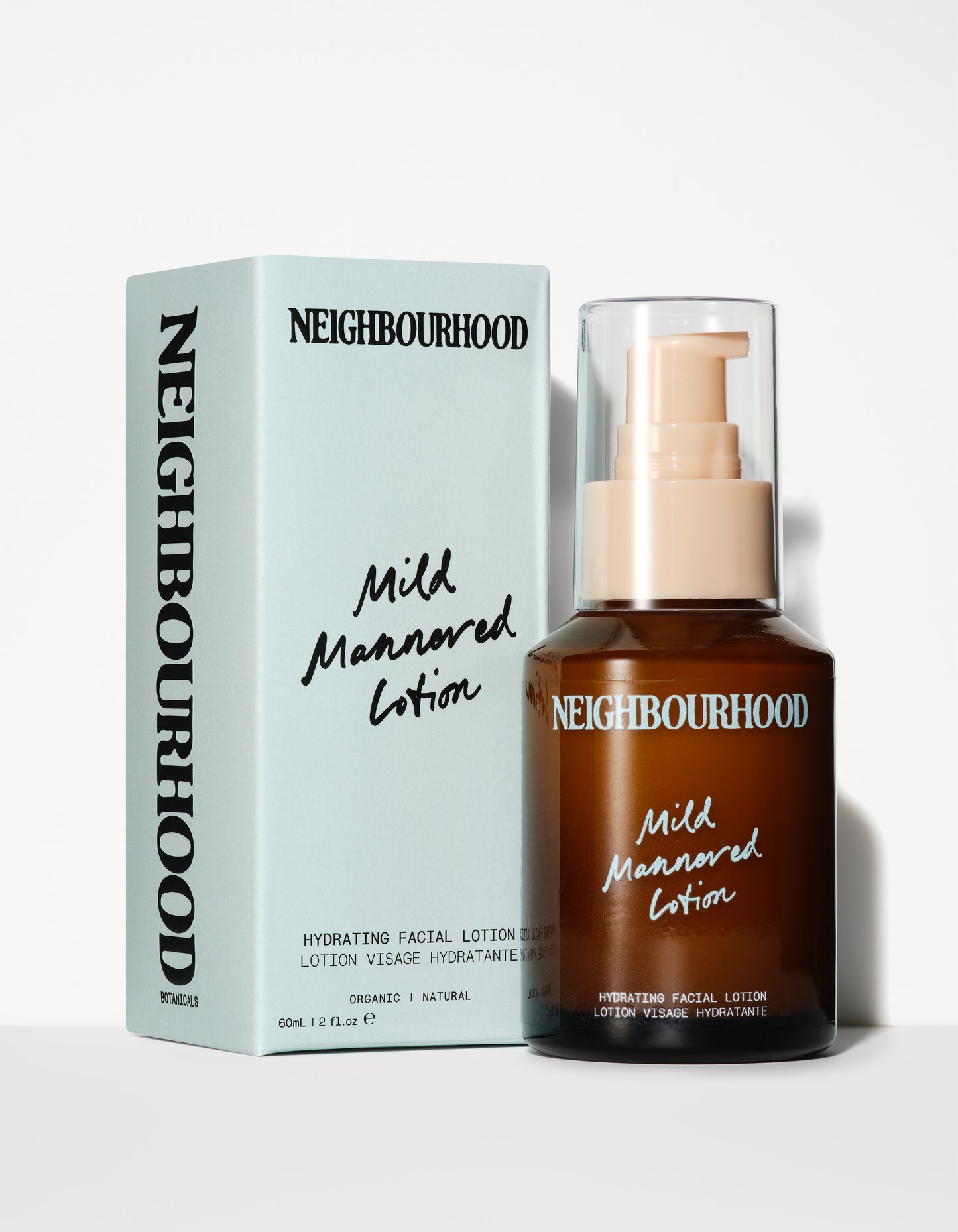A brown glass bottle with a cream pump dispenser and clear cap labeled "Neighbourhood Mild Mannered Lotion," placed next to a soft blue box with bold black typography. The packaging states it is a hydrating facial lotion made with organic, natural ingredients.