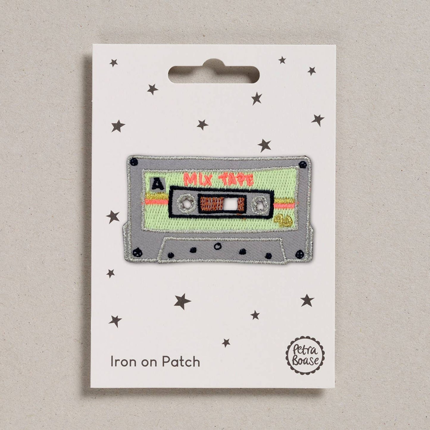 An embroidered iron-on patch shaped like a retro cassette tape, featuring a light grey body, neon green label, and red "Mix Tape" text. Packaged on a cream backing card with black stars and Petra Boase branding.