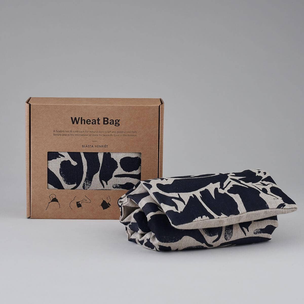 Wheat bag with black and white pattern next to its cardboard packaging on a gray background
