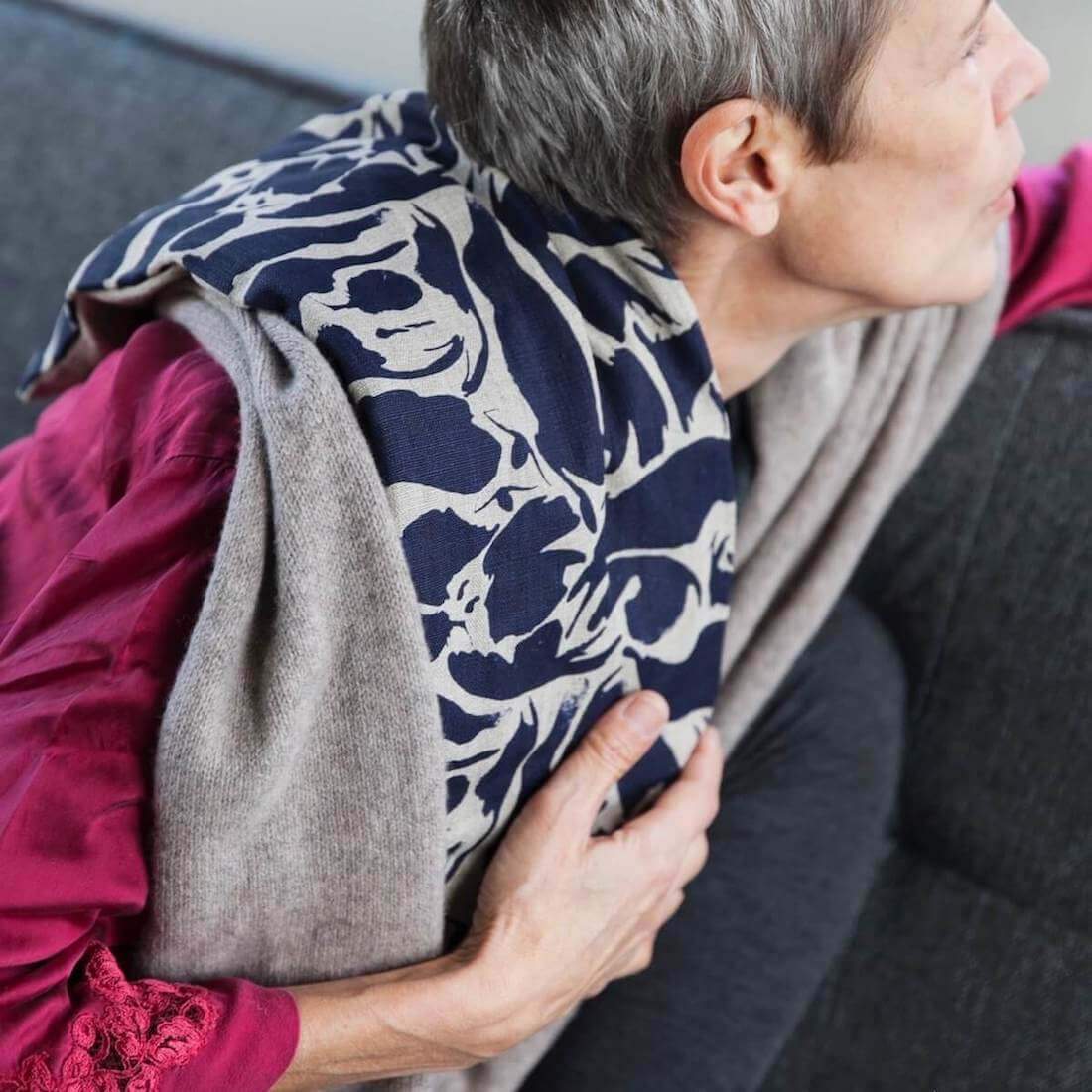 Person wearing a patterned wheat bag on the shoulder with a neutral background
