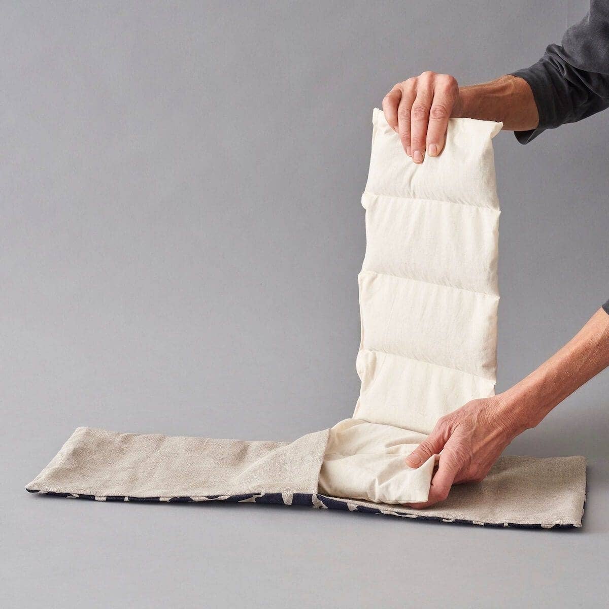 Person inserting white wheat bags into the printed sleeve on a grey background