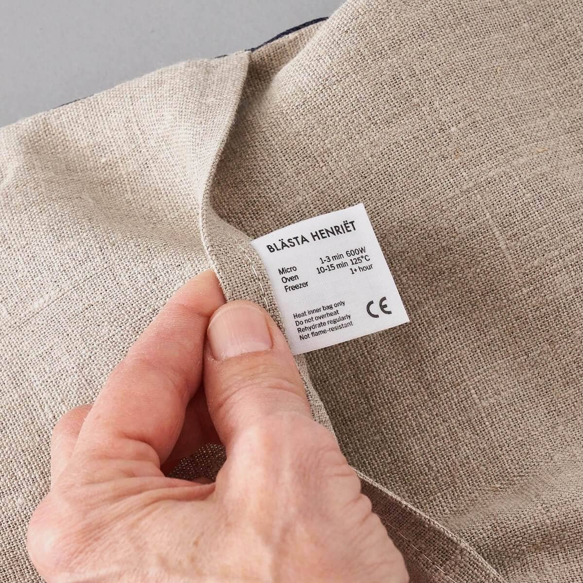 Hand holding a label on beige fabric with text and symbols.