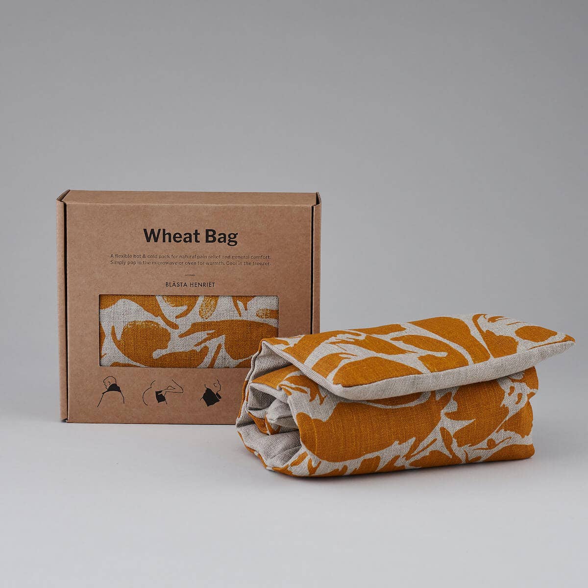 Wheat bag with floral pattern next to its packaging box on a gray background