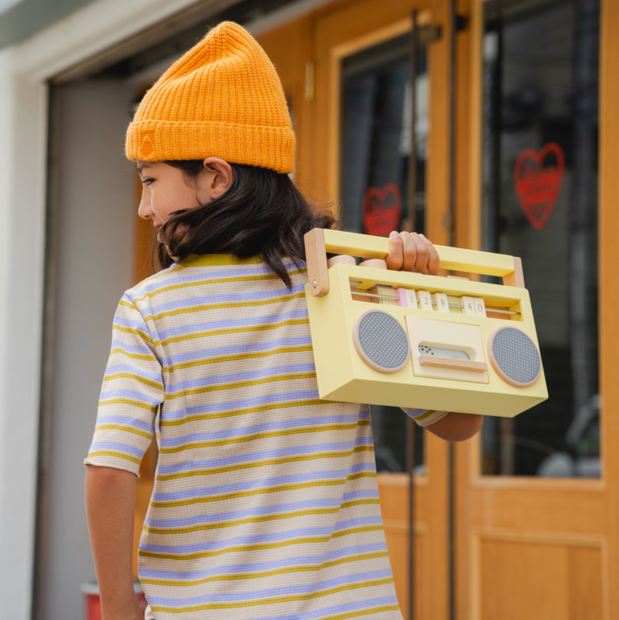 Person wearing a yellow beanie and striped shirt, holding a toy boombox outdoors.